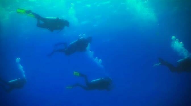 Scuba divers, motivated by a deep desire, submerged in deep blue waters, illuminated by sunlight from above.