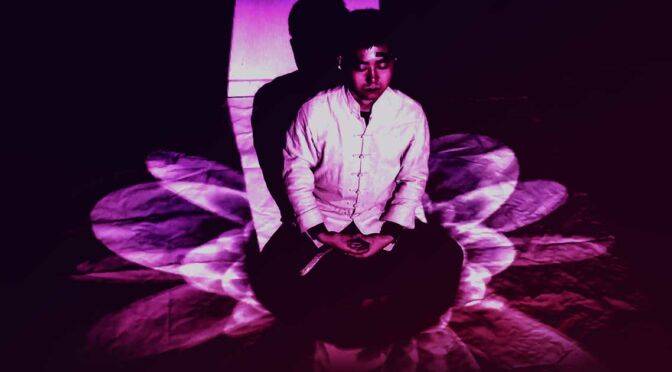 A person meditating cross-legged with a serene expression, surrounded by beautiful purple light patterns.